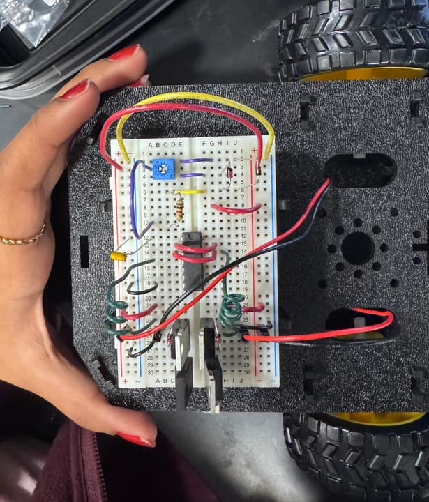 Hand holding a wheeled robot chassis with a breadboard circuit of jumper wires, a chip and a potentiometer